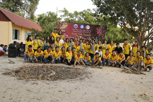 A large group of volunteers in yellow shirts in front of a Xuân Tình Nguyện banner