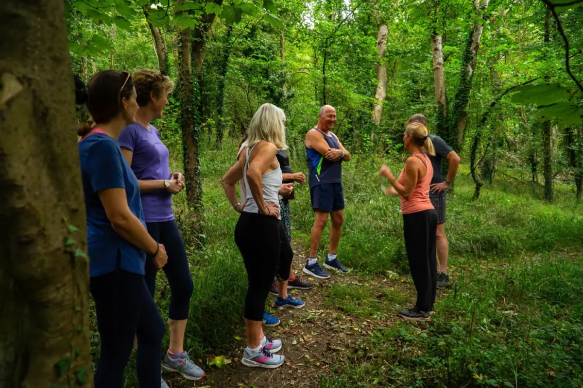 A group of guests standing together on a woodland path at Combe Grove, mid-conversation on a walk