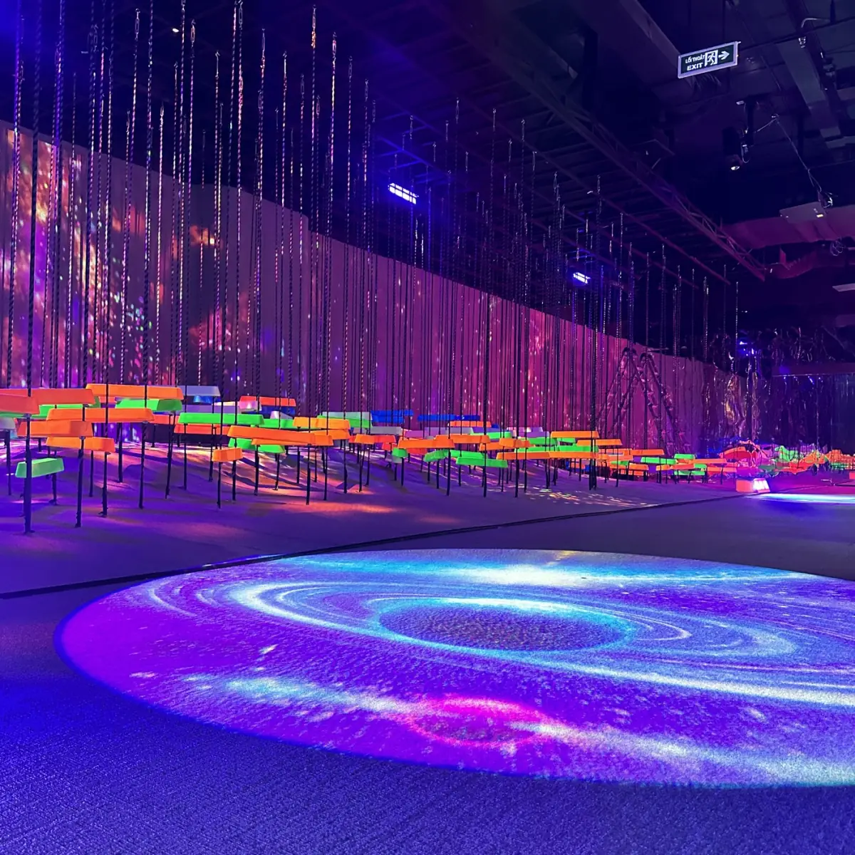 The interactive light floor at JP World, GiGa Mall — projected galaxies across a dark room lit in violet and orange